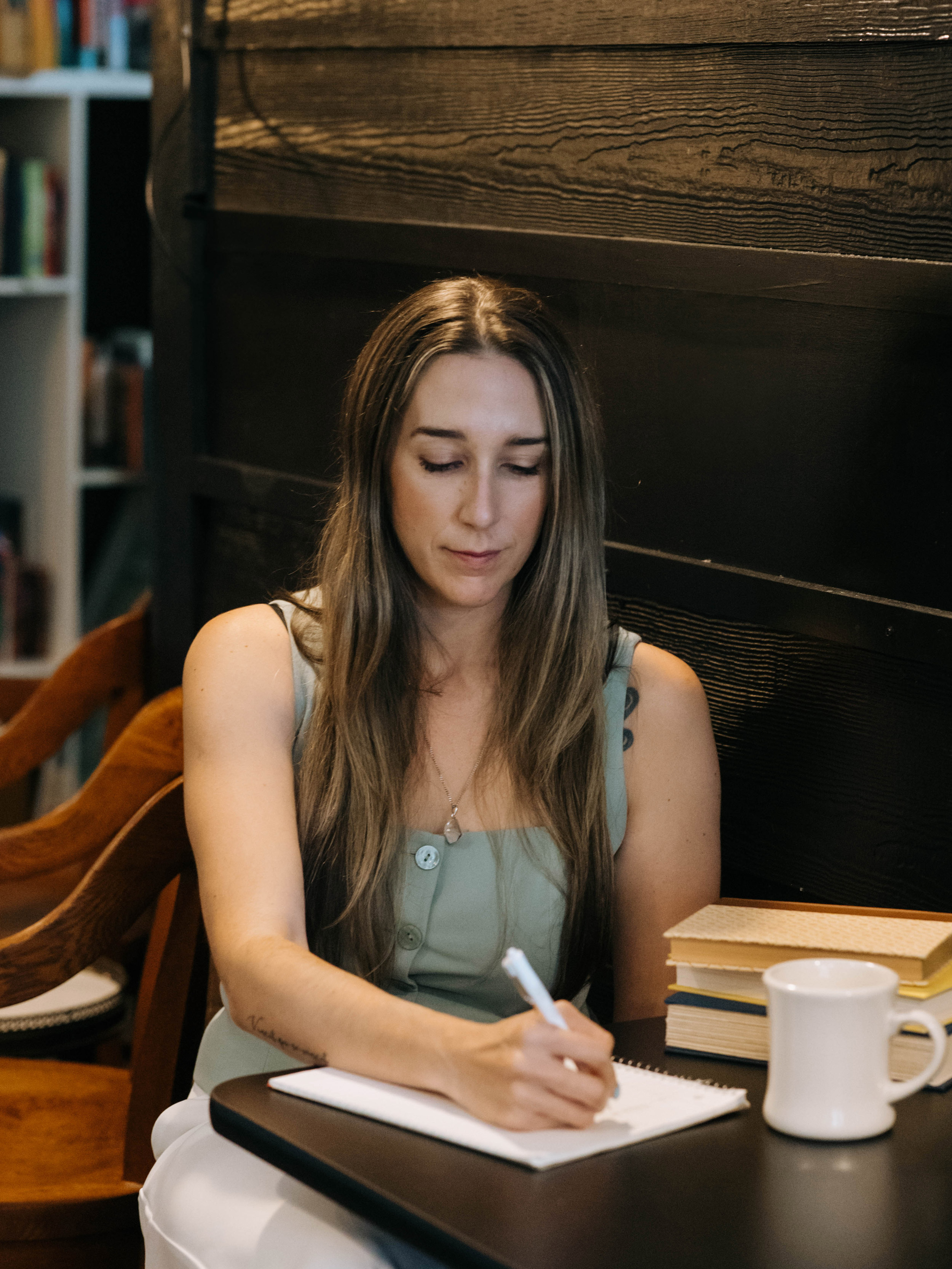 Camila Hurst in a coffee library on a table writing and surounded by books and cup of coffee